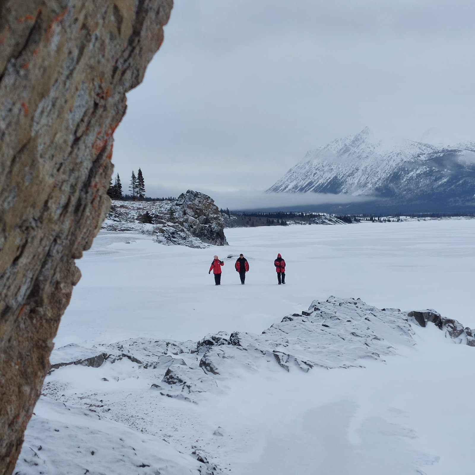 Three travellers walking on a frozen lake below the mountains