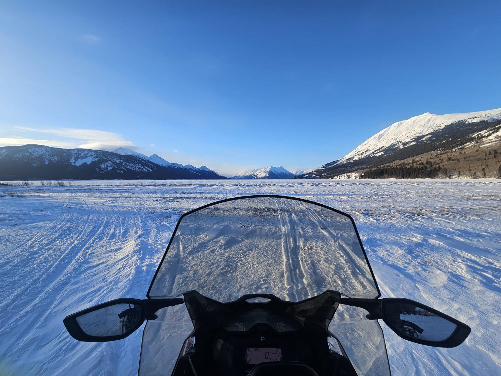 Snowmobile view across a frozen lake and mountains